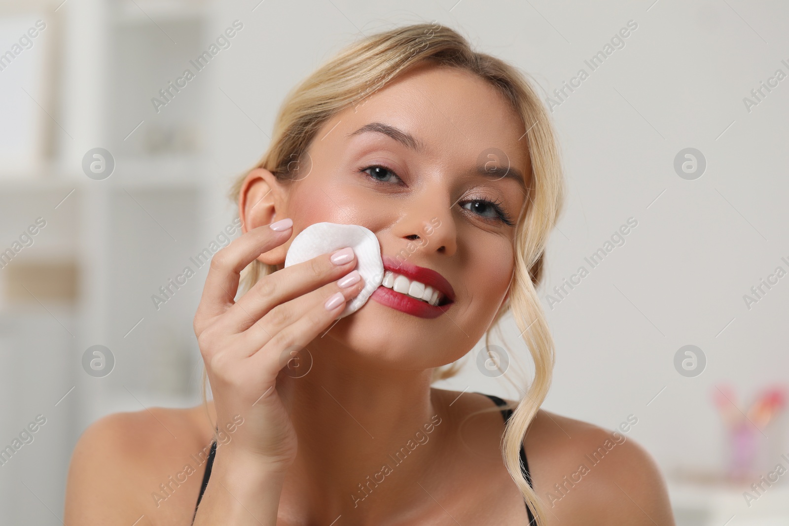 Photo of Smiling woman removing makeup with cotton pad indoors, closeup