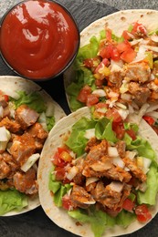 Delicious tacos with vegetables, meat and ketchup on table, top view