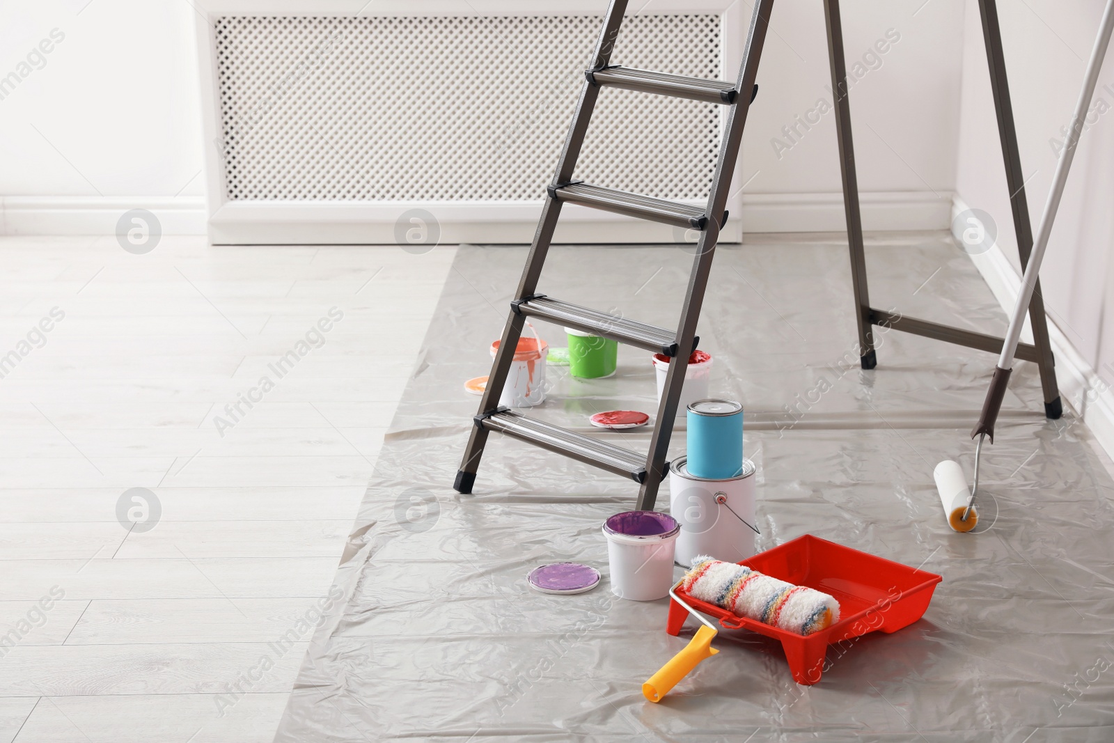 Photo of Different paints and decorator's tools near ladder indoors, space for text