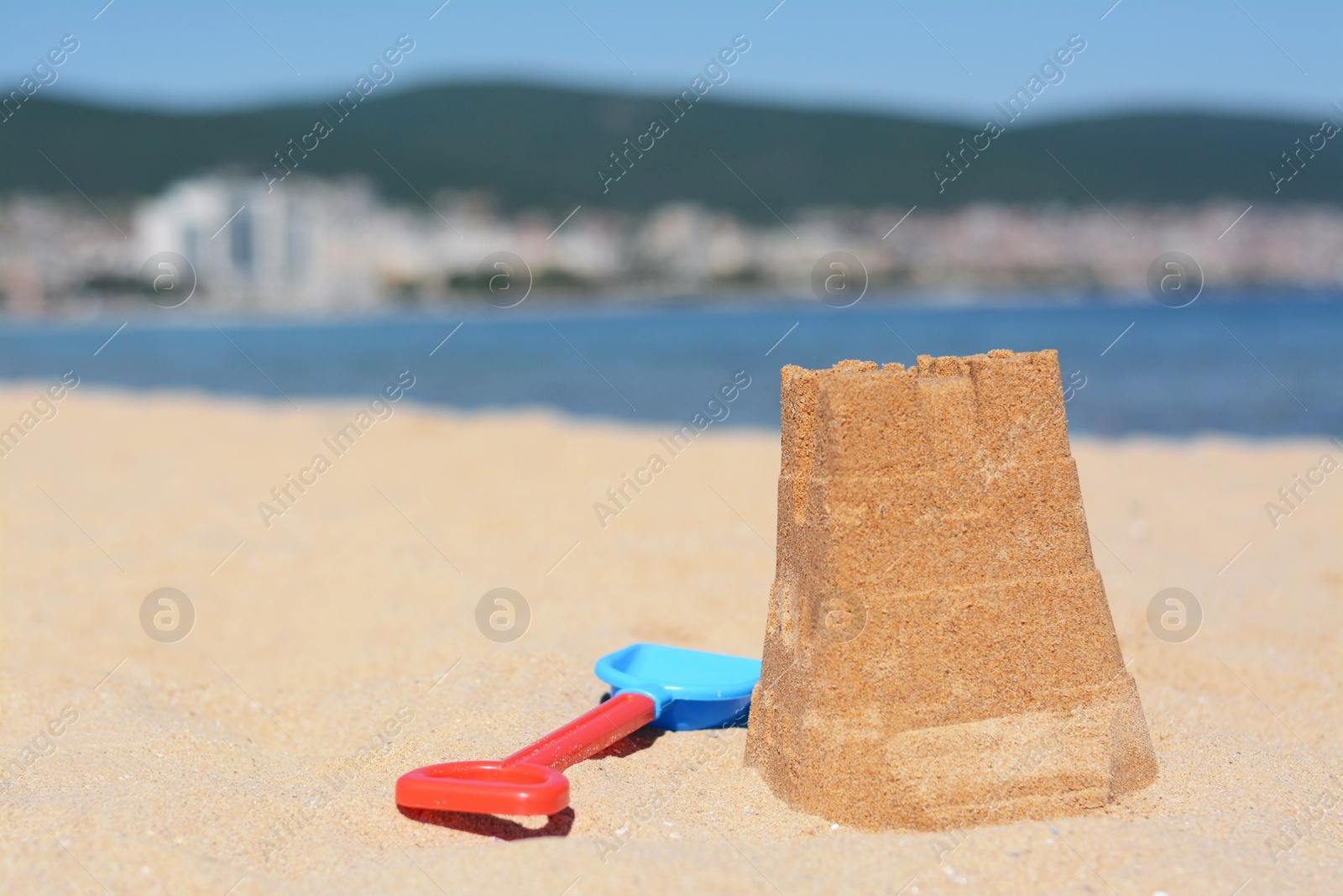 Photo of Sand castle and child plastic shovel on beach near sea. Space for text