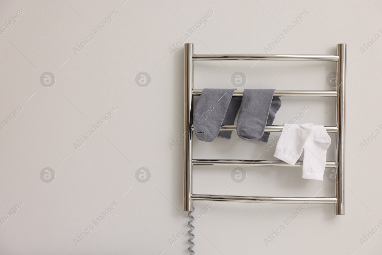 Photo of Heated towel rail with socks on white wall, space for text