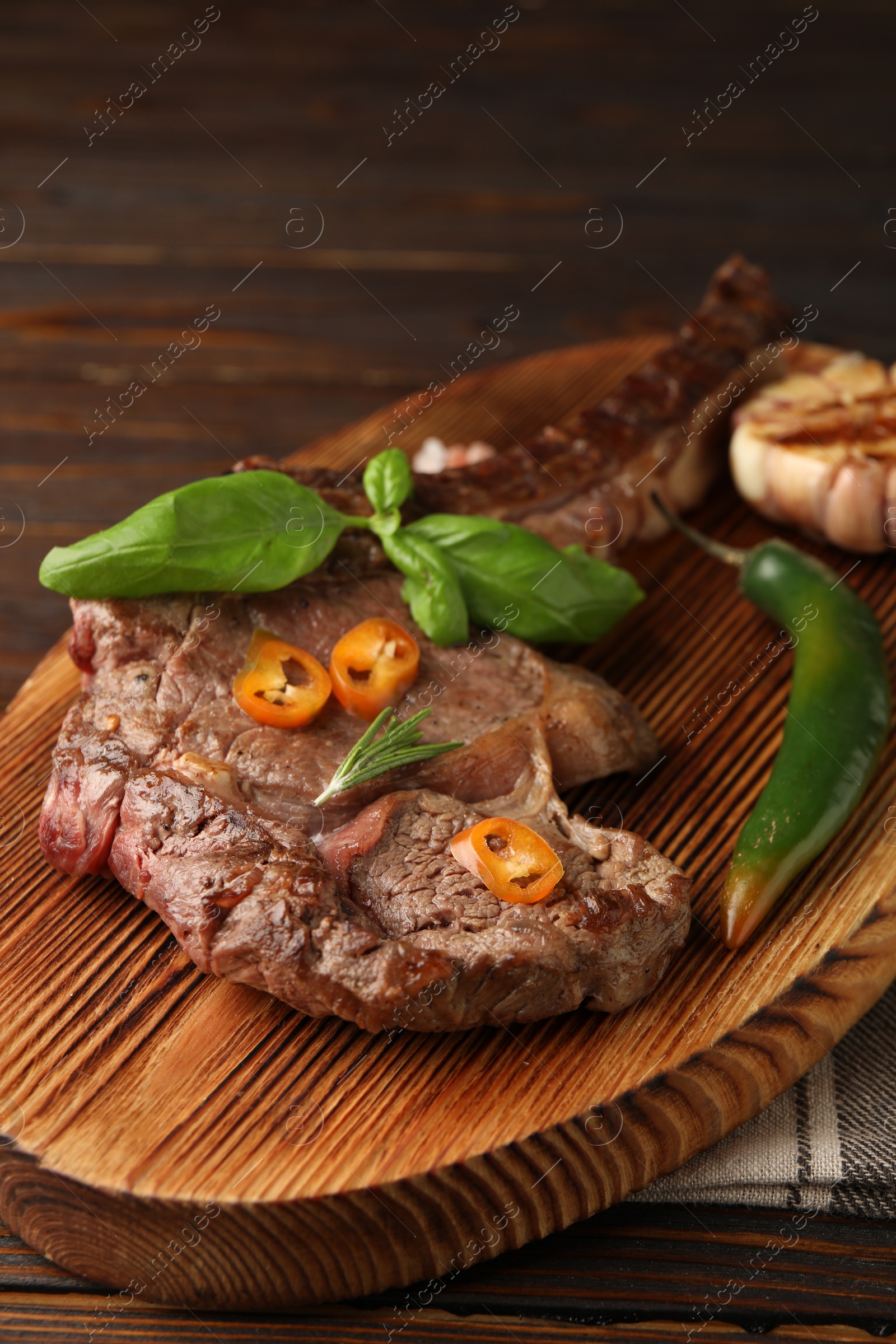 Photo of Delicious fried beef meat with garlic and chili pepper on wooden table