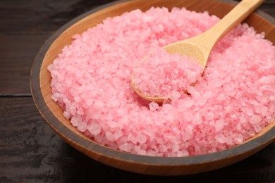 Photo of Bowl and spoon with pink sea salt on wooden table, closeup