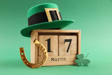 Photo of St. Patrick's day - 17th of March. Wooden block calendar, leprechaun hat, golden horseshoe and decorative clover leaf on green background