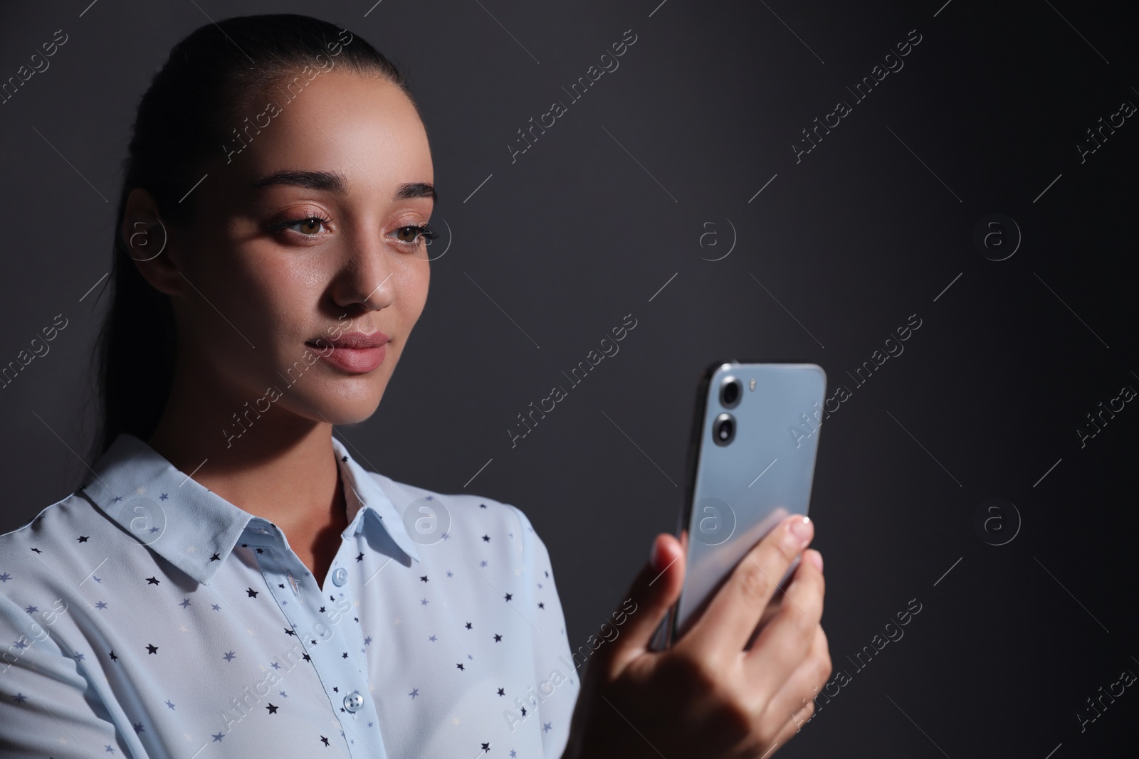 Photo of Young woman unlocking smartphone with facial scanner on black background. Biometric verification