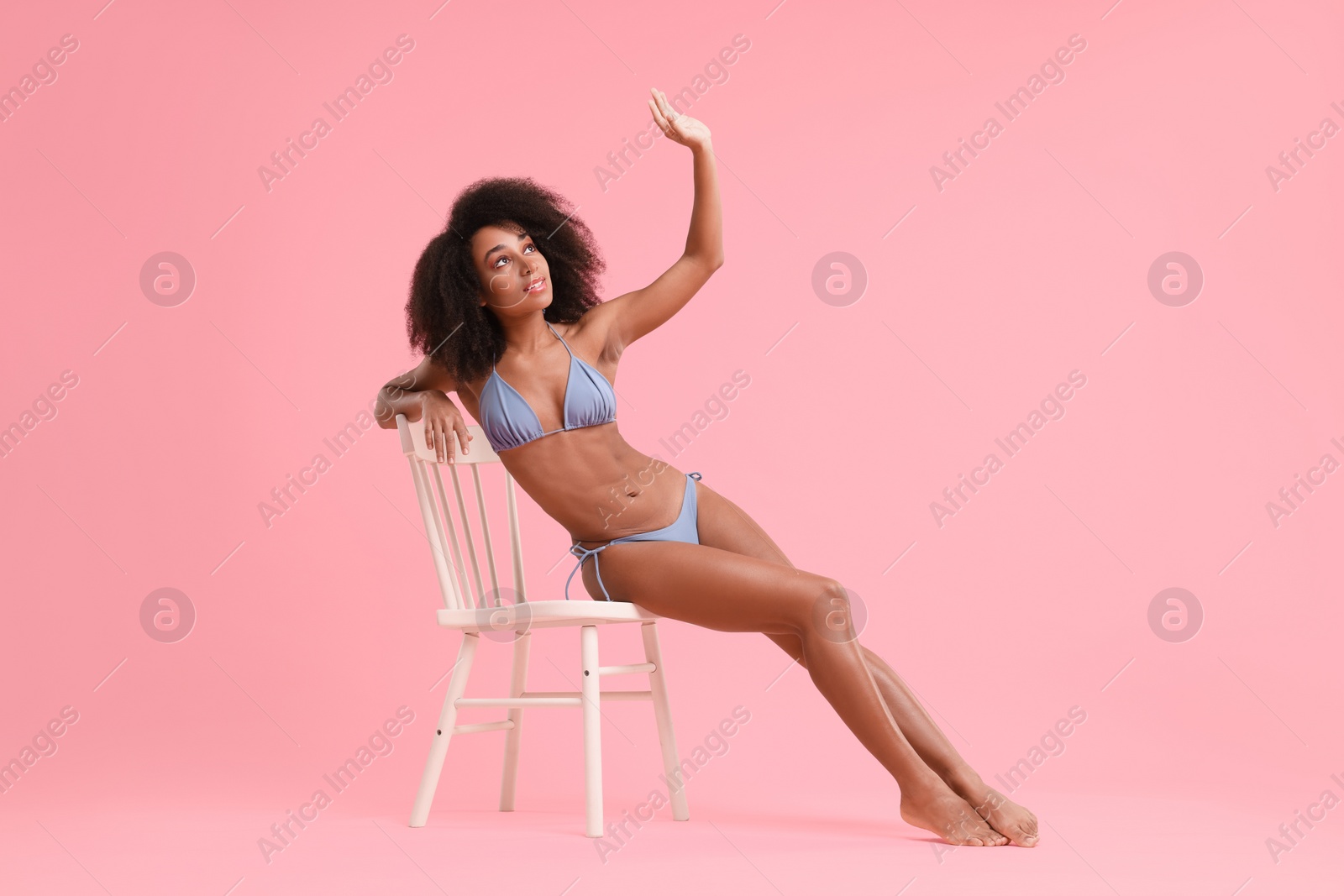 Photo of Beautiful woman in stylish bikini posing on chair against pink background