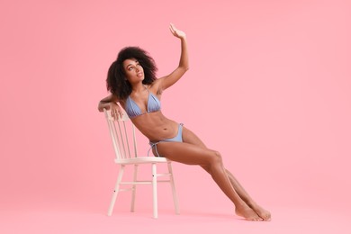 Beautiful woman in stylish bikini posing on chair against pink background