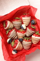 Box with delicious chocolate covered strawberries and blueberries on white table, top view