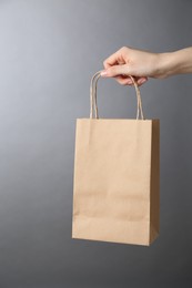 Photo of Woman holding kraft paper bag on grey background, closeup. Mockup for design