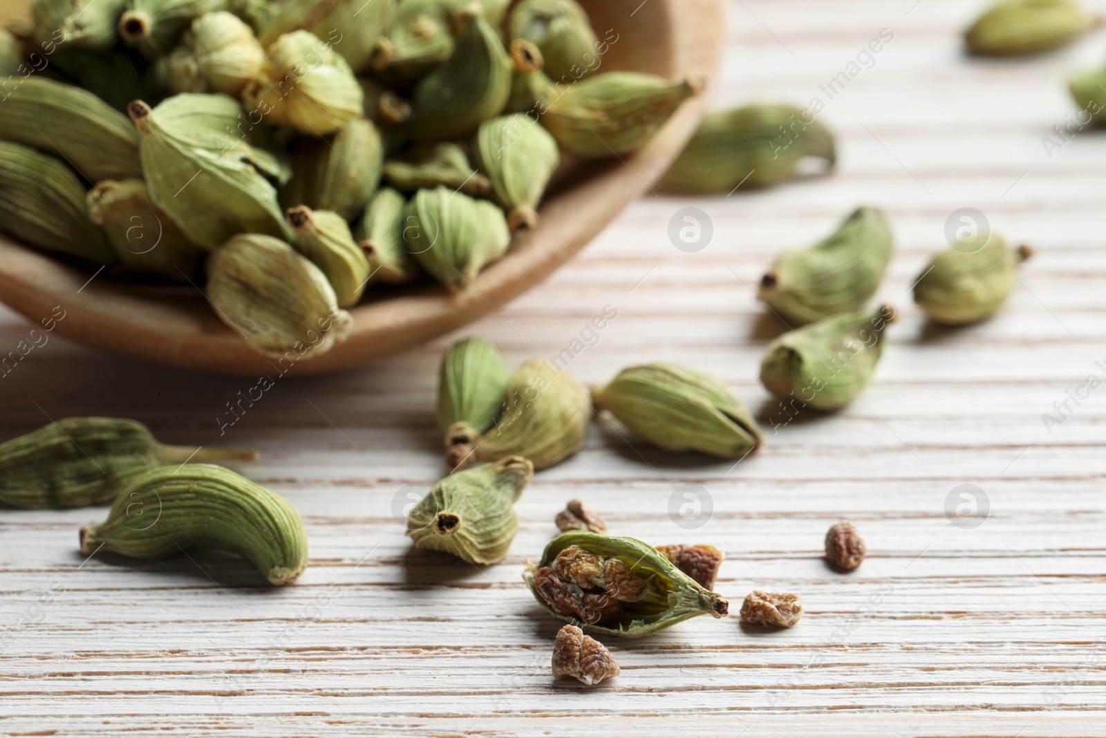 Photo of Spoon with dry cardamom pods on white wooden table, closeup