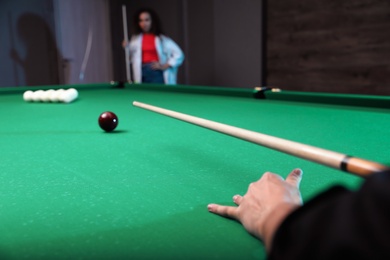 Young man playing billiard and blurred African-American woman on background