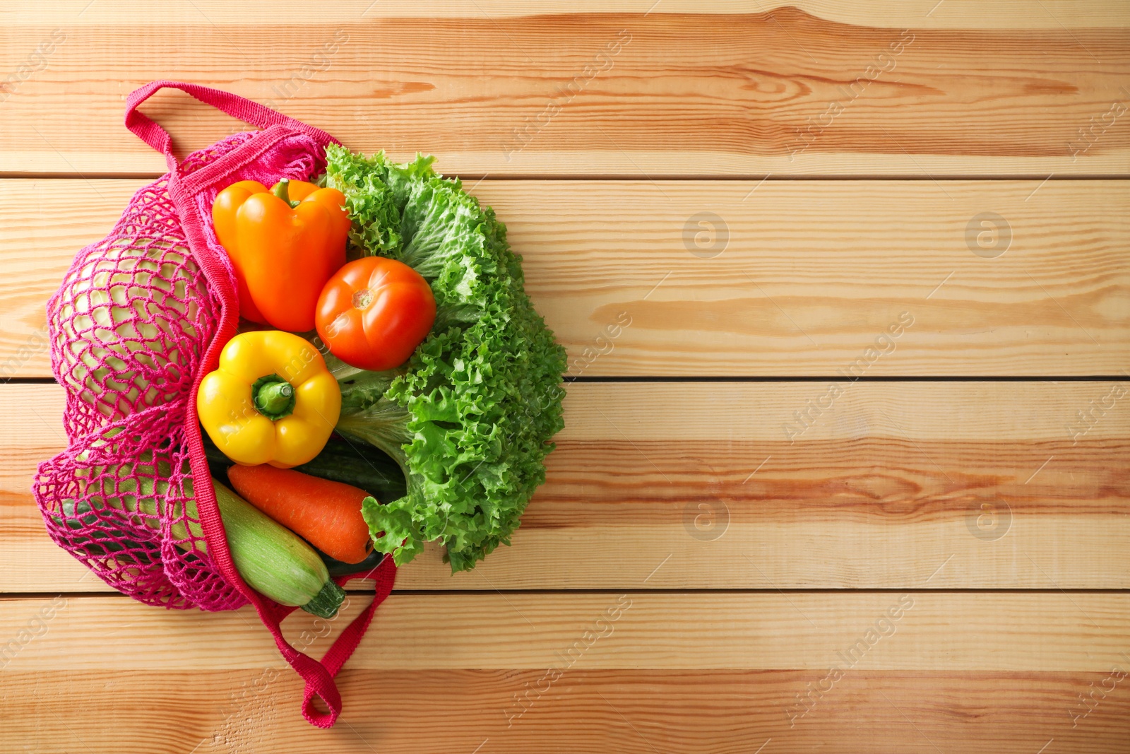 Photo of Net bag with vegetables on wooden table, top view. Space for text