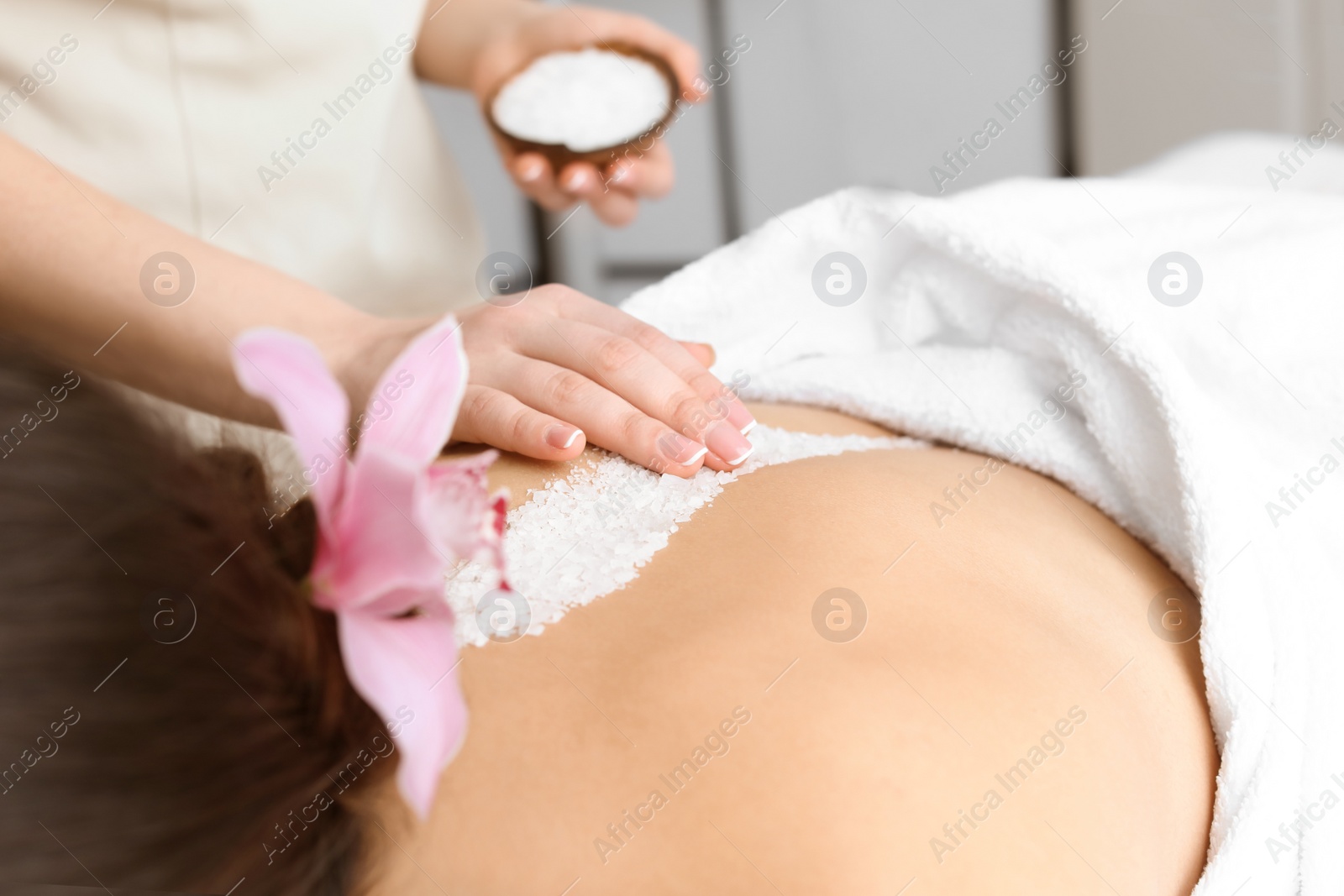 Photo of Young woman having body scrubbing procedure with sea salt in spa salon, closeup