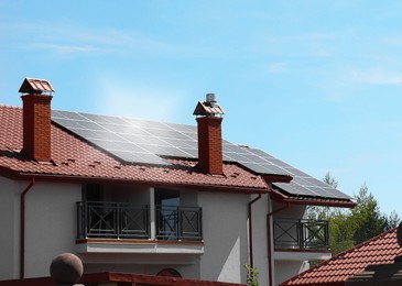 House with installed solar panels on roof under blue sky. Alternative energy source