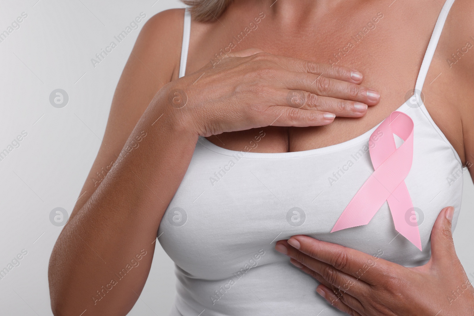 Photo of Woman with pink ribbon on white background, closeup. Breast cancer awareness