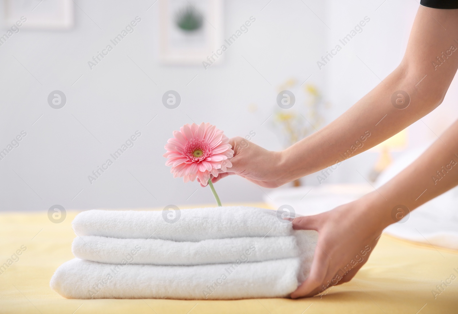 Photo of Young maid putting flower on stack of towels in hotel room