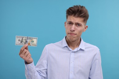 Photo of Upset man with dollar banknote on light blue background