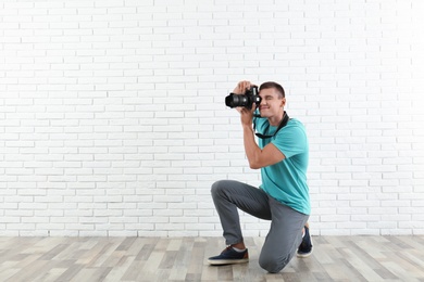 Young professional photographer taking picture near brick wall. Space for text