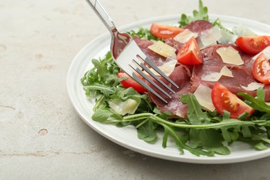 Photo of Eating delicious bresaola salad at light grey textured table, closeup. Space for text