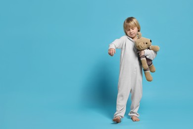 Boy in pajamas with toy bear sleepwalking on light blue background, space for text