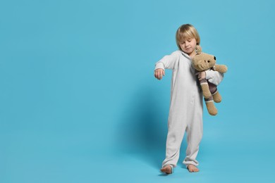 Photo of Boy in pajamas with toy bear sleepwalking on light blue background, space for text