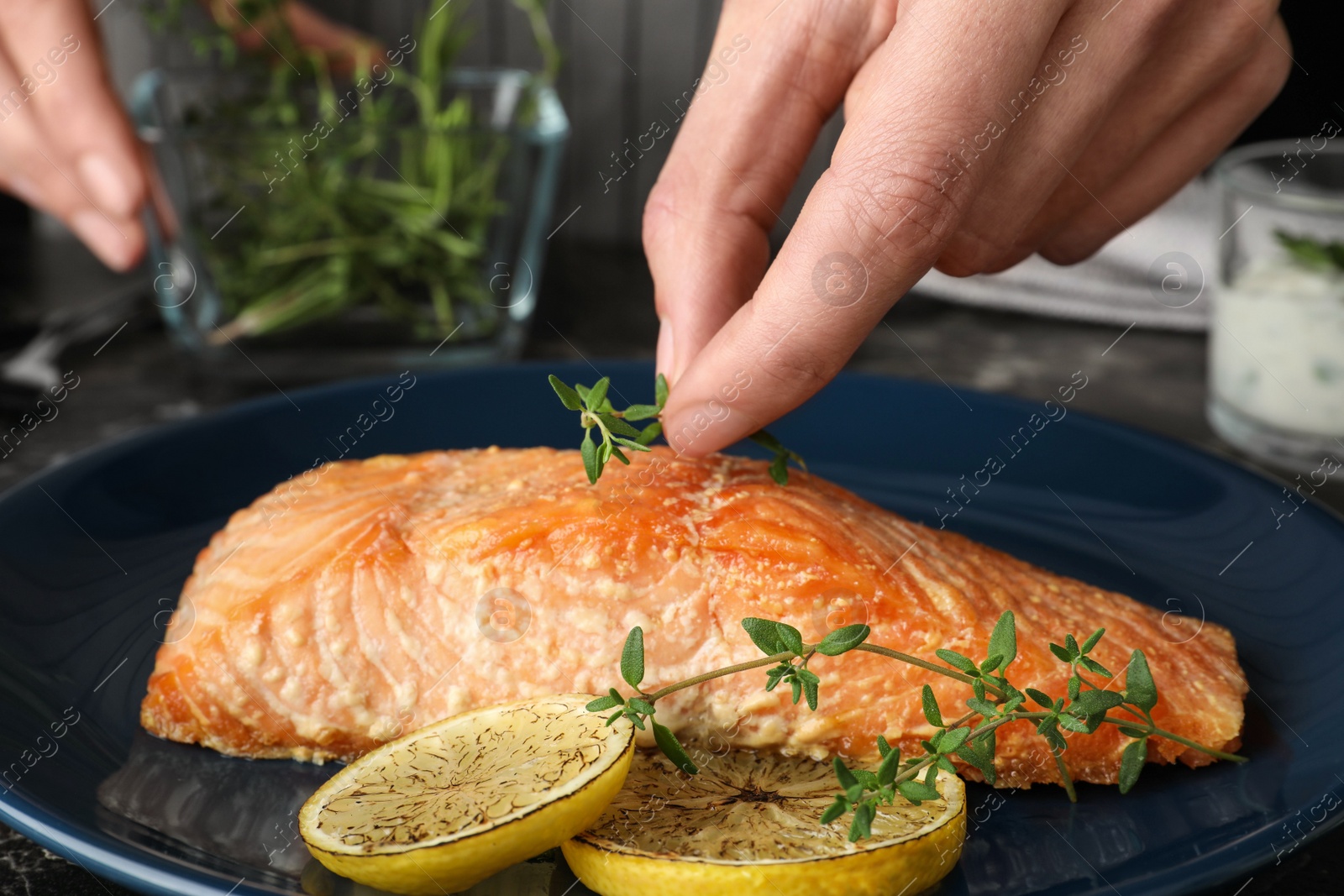 Photo of Woman adding thyme to cooked red fish on table, closeup