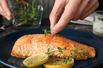 Woman adding thyme to cooked red fish on table, closeup