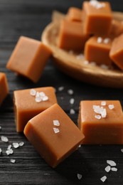 Photo of Yummy caramel candies and sea salt on black wooden table, closeup
