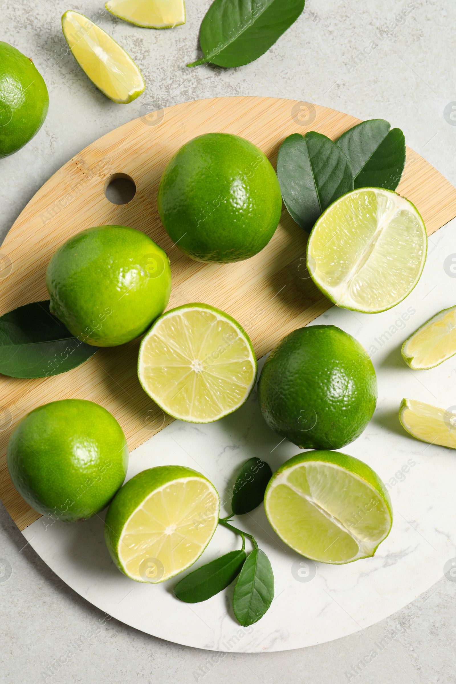 Photo of Fresh ripe limes and leaves on light table, top view