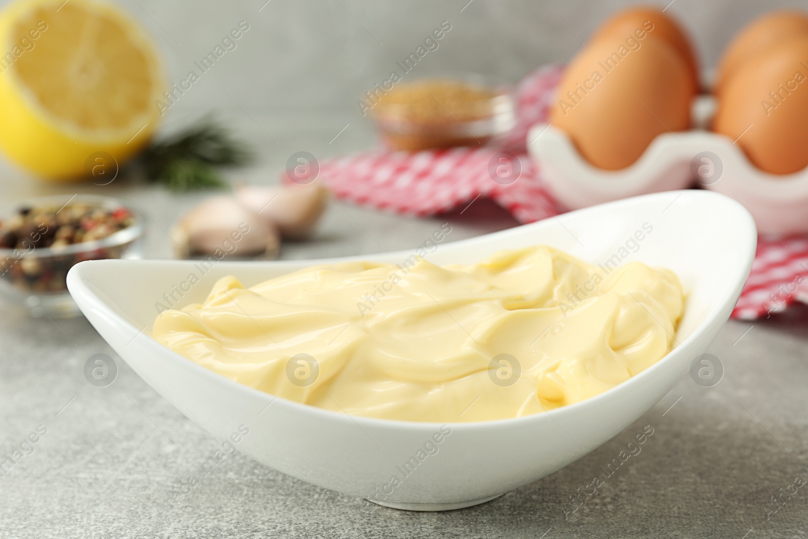 Photo of Delicious homemade mayonnaise near ingredients on grey table, closeup