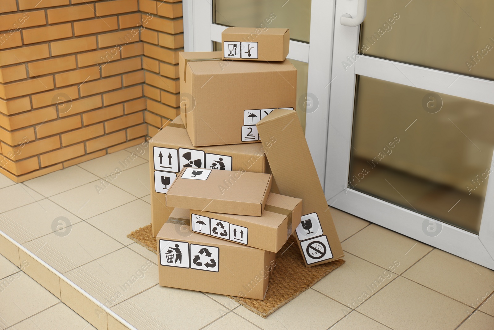 Photo of Cardboard boxes with different packaging symbols on door mat near entrance. Parcel delivery