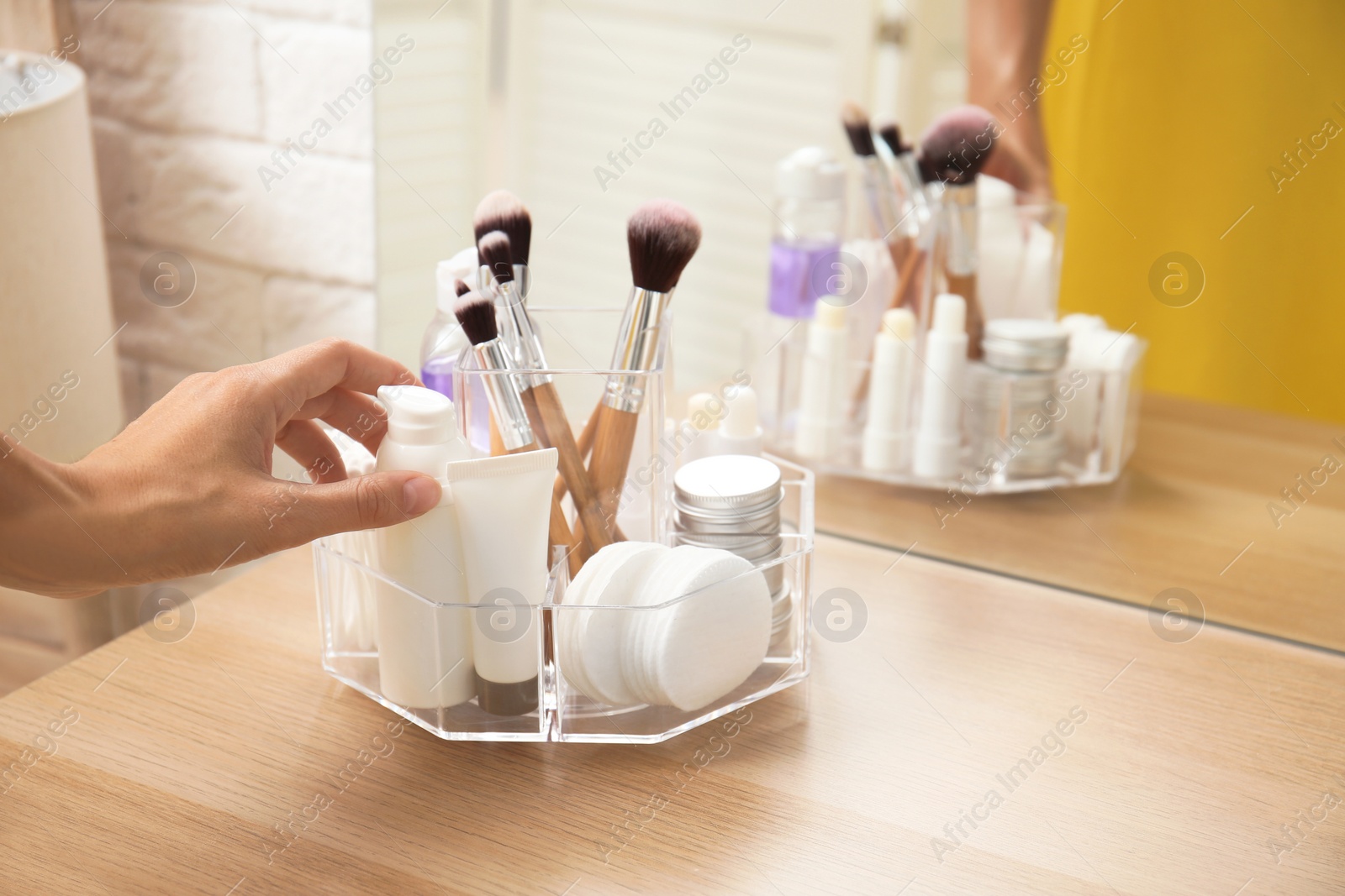 Photo of Woman taking bottle of cream from organizer for cosmetic products on table