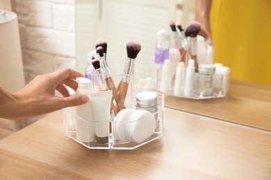 Photo of Woman taking bottle of cream from organizer for cosmetic products on table