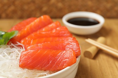 Photo of Delicious salmon sashimi served with funchosa and parsley on wooden table, closeup