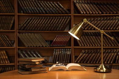 Photo of Lamp, books and glasses on wooden table in library