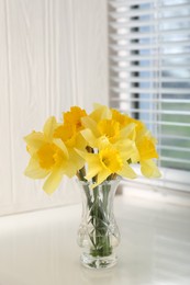 Photo of Beautiful yellow daffodils in vase on windowsill. Space for text