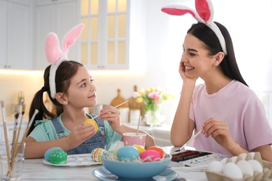 Photo of Happy mother with her cute daughter painting Easter eggs at table in kitchen