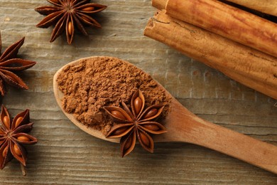 Spoon with cinnamon powder, sticks and star anise on wooden table, flat lay