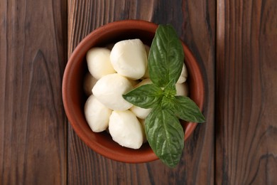 Photo of Tasty mozarella balls and basil leaves in bowl on wooden table, top view