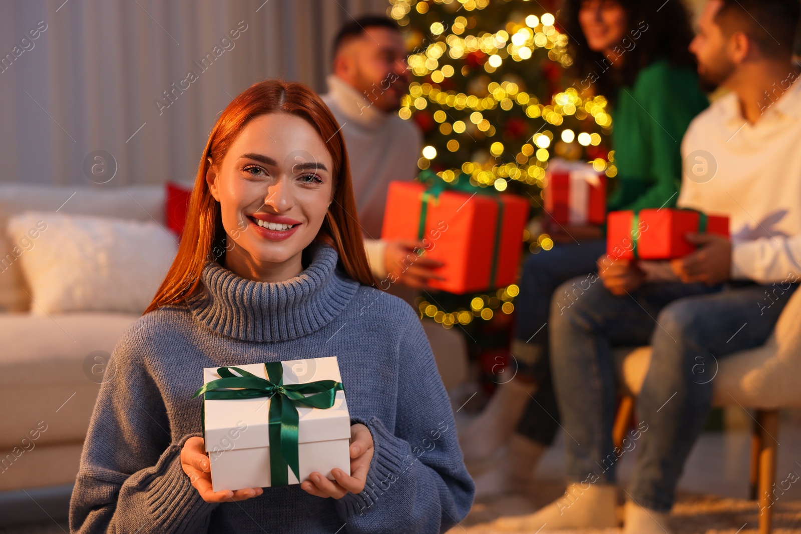 Photo of Christmas celebration in circle of friends. Happy young woman with gift box at home, selective focus