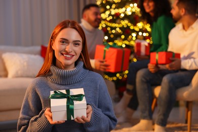 Christmas celebration in circle of friends. Happy young woman with gift box at home, selective focus