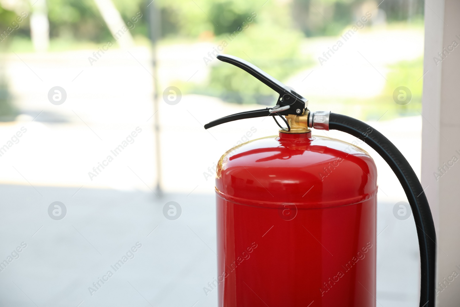 Photo of Fire extinguisher near window indoors, closeup. Space for text