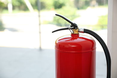 Photo of Fire extinguisher near window indoors, closeup. Space for text