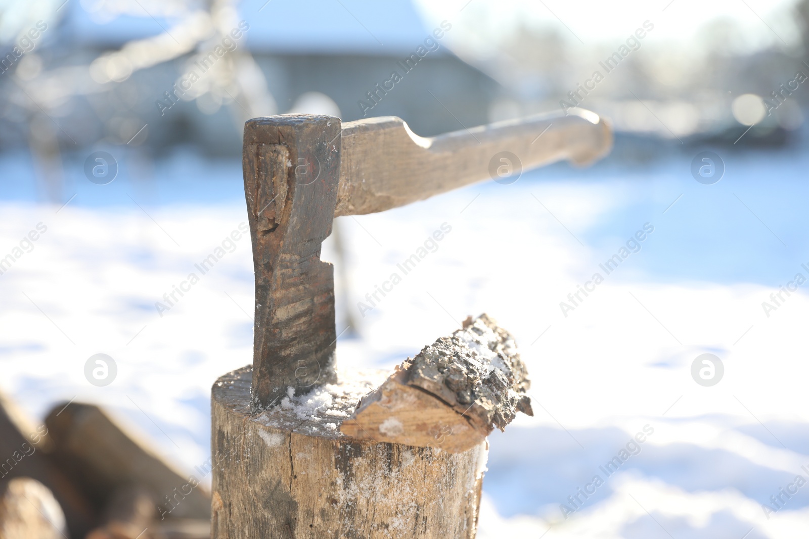 Photo of Metal axe in wooden log on sunny winter day, closeup