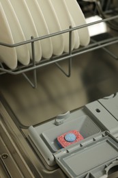 Photo of Open dishwasher with detergent tablet and plates, closeup