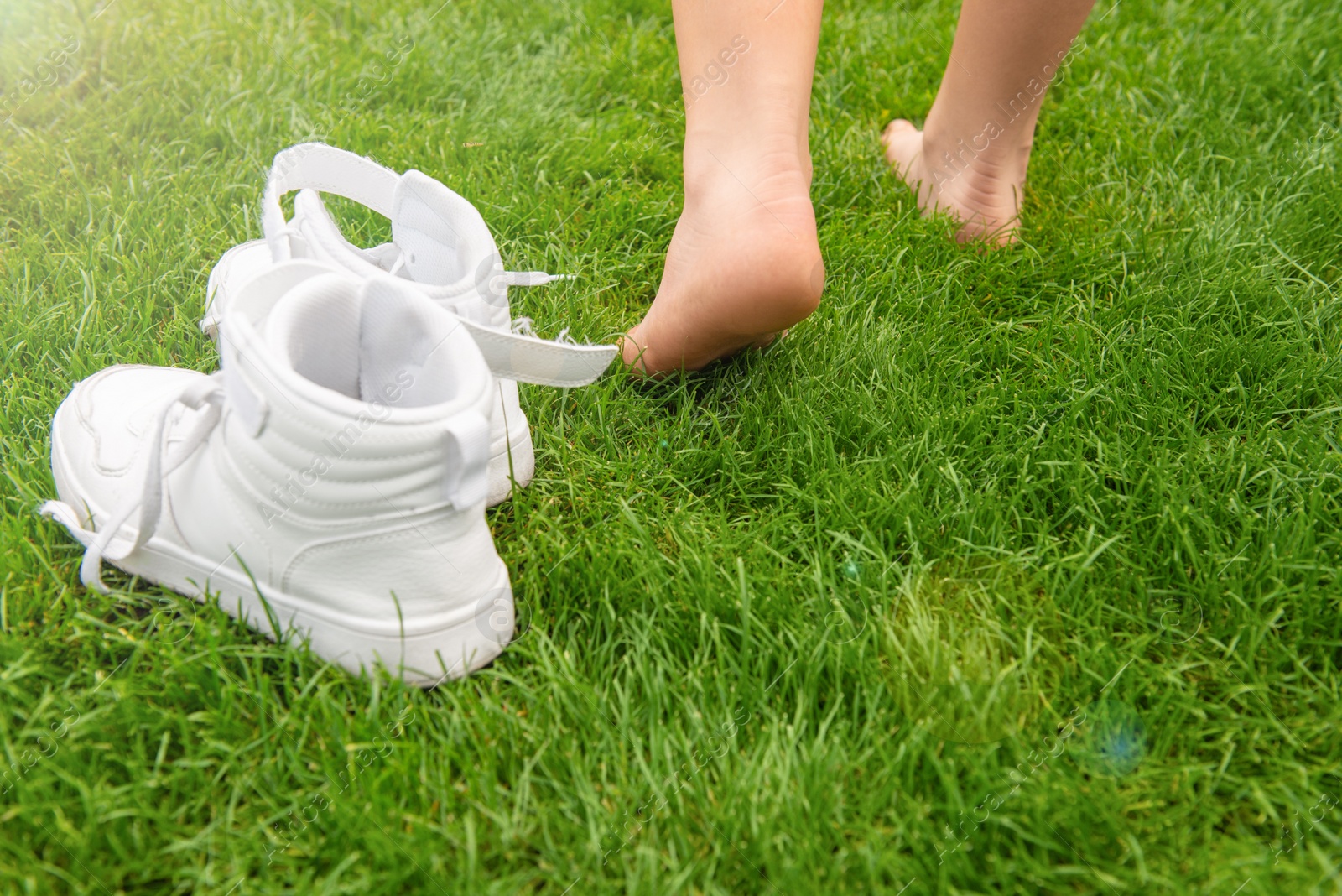 Photo of Woman leaving her sneakers and walking away barefoot on green grass, closeup