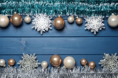 Bright tinsel and Christmas decor on light blue wooden background, flat lay. Space for text