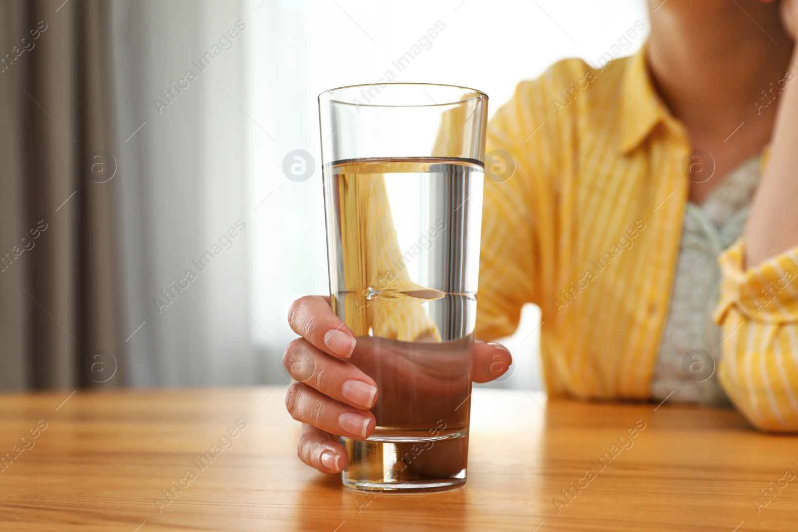 Photo of Woman holding glass of water at wooden table, closeup. Refreshing drink