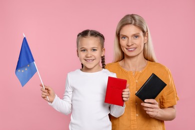 Photo of Immigration. Happy woman with her daughter holding passports and flag of European Union on pink background