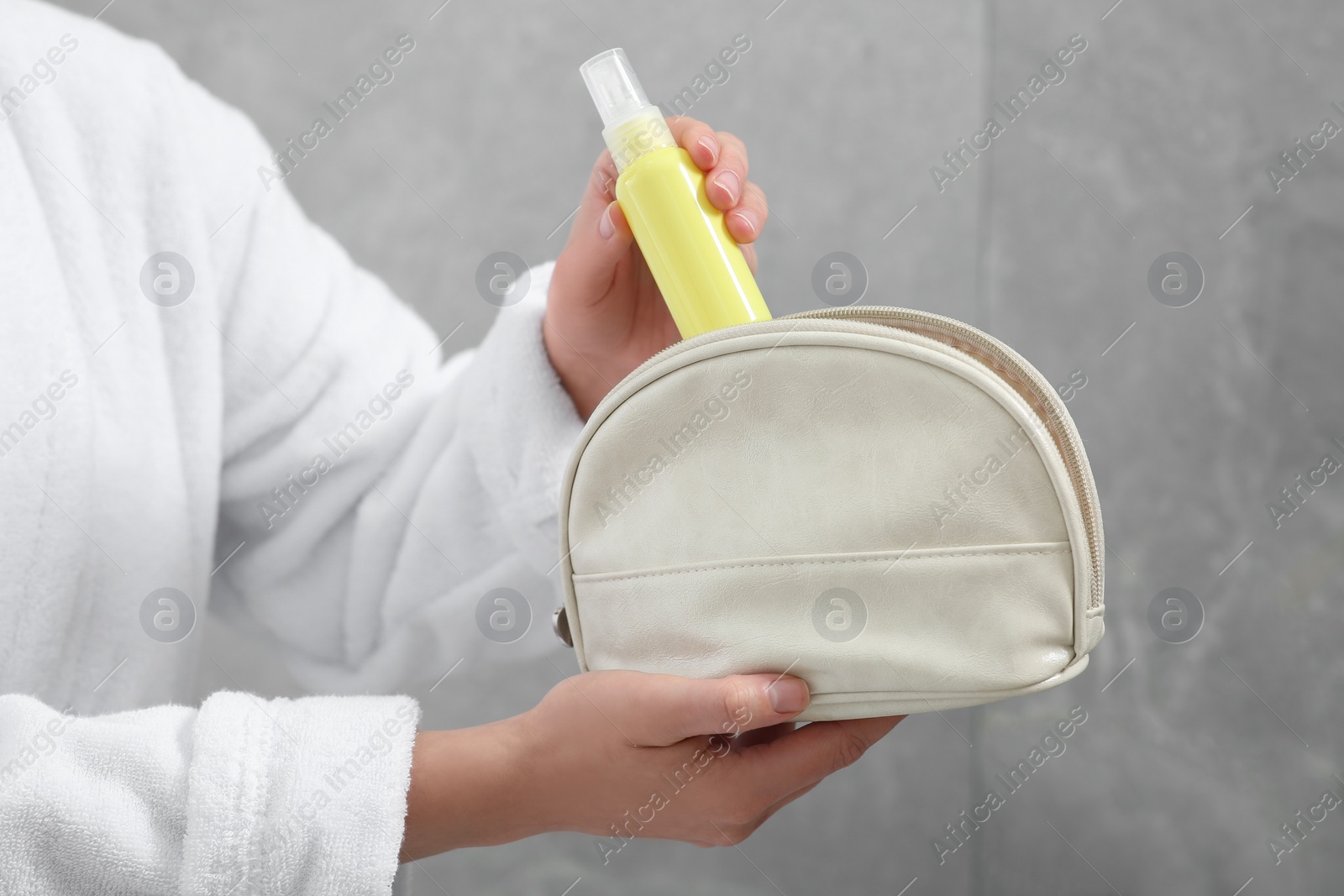 Photo of Woman packing cosmetic travel kit near grey wall closeup. Bath accessories